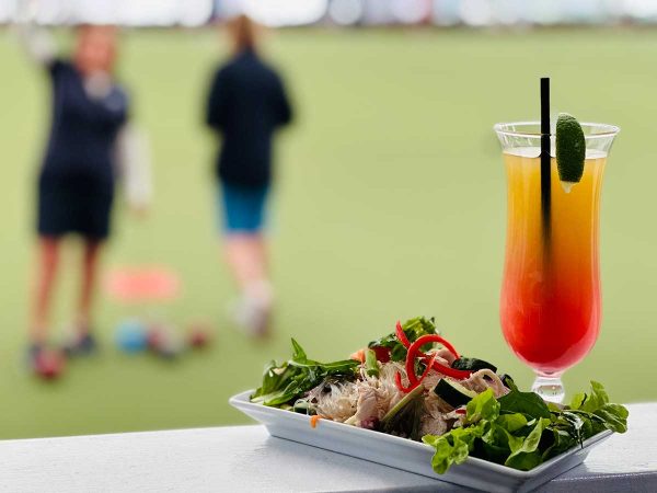 two bowlers in the background with a plate of food and a cocktail in the foreground